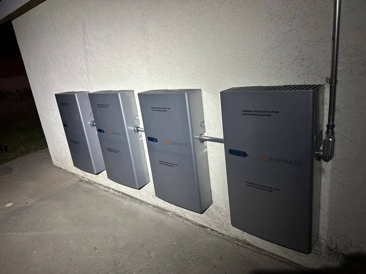 Four Enphase IQ Battery 5P units mounted side by side on an exterior wall, with conduit running between them